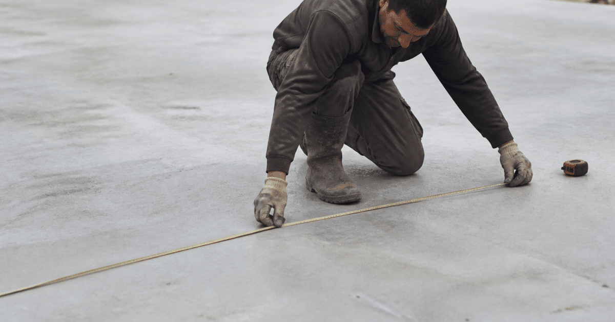 Ouvrier mesure une dalle beton grise horizontale au sol