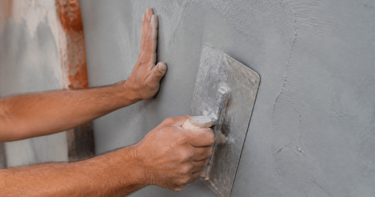 Mains appliquant revetement lisse sur surface murale grise